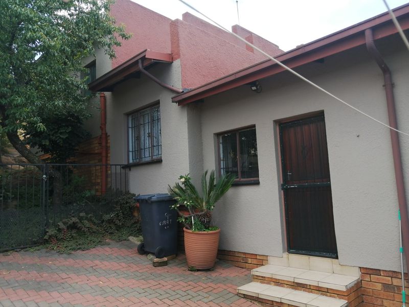 Rear exterior view of the property featuring a textured facade, security bars on windows, a security gate, and brick paved courtyard area.