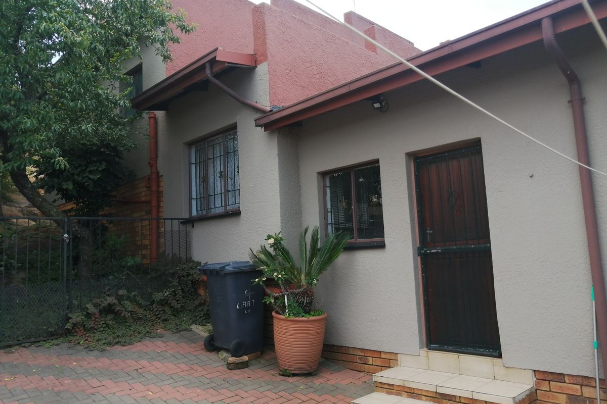 Rear exterior view of the property featuring a textured facade, security bars on windows, a security gate, and brick paved courtyard area.