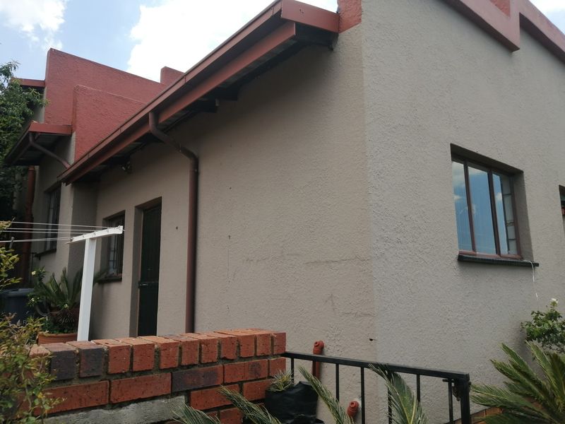 A view of the rear exterior facade featuring textured plaster walls, metal guttering, and a brick boundary wall.