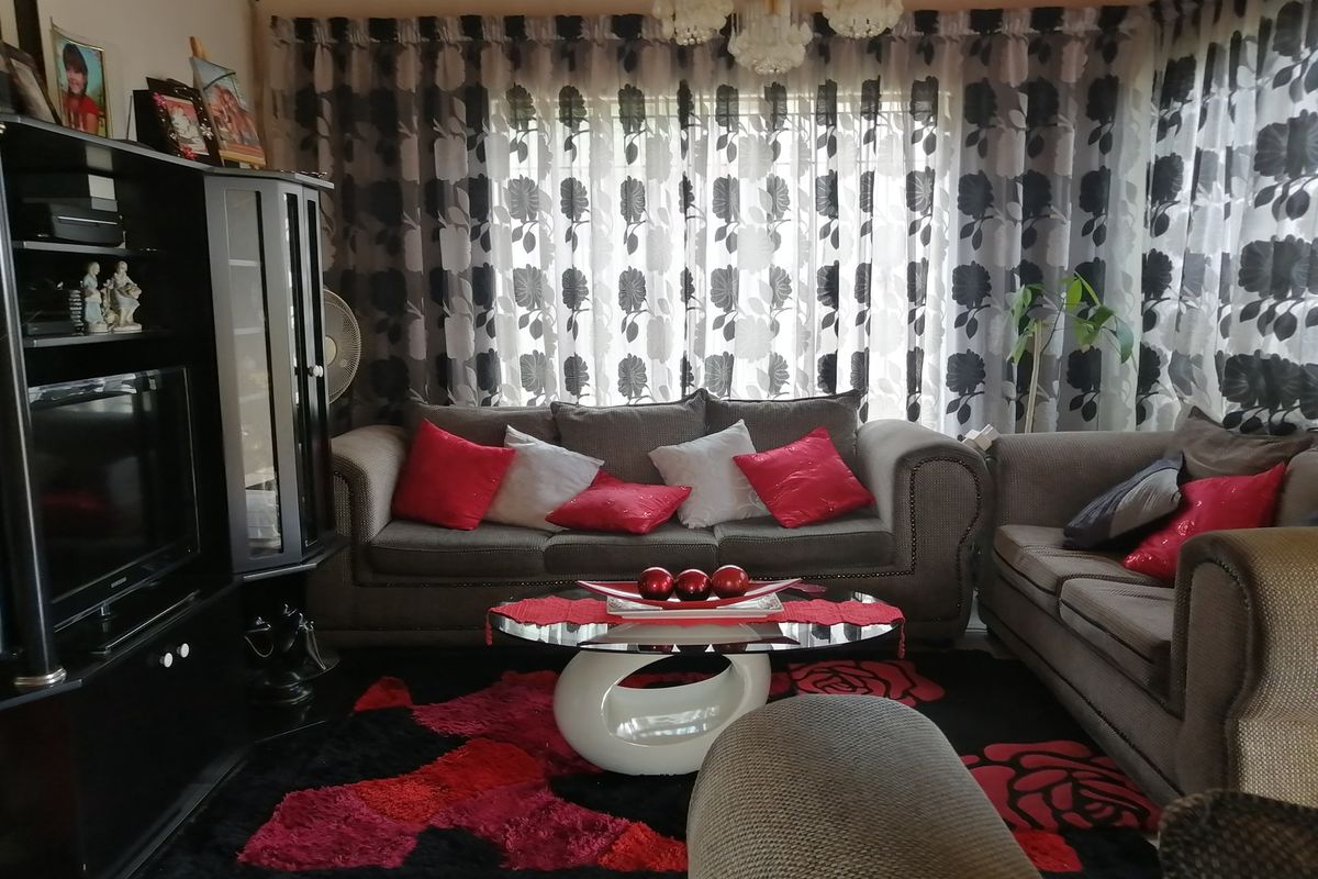A cozy living room featuring a central chandelier and large window with patterned curtains, providing a comfortable space for relaxation.