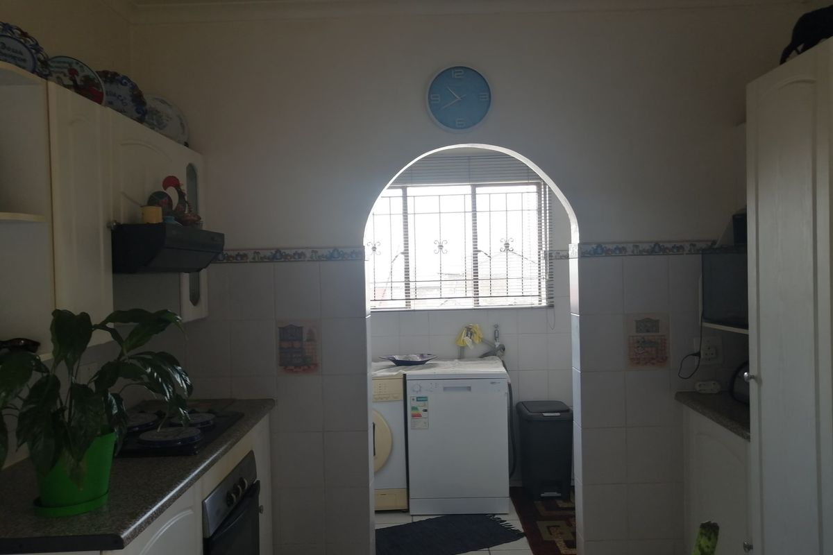 A functional kitchen featuring built-in cabinetry, integrated oven and hob, and a separate scullery area accessed through a classic arched doorway.