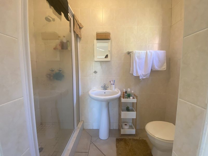 A functional bathroom featuring a pedestal basin, a glass-enclosed shower, and neutral ceramic tiling throughout.