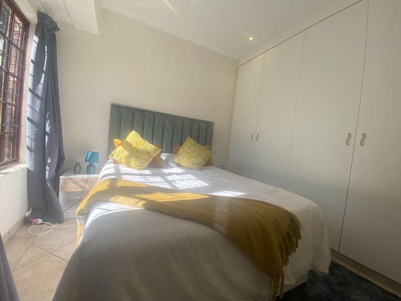A bright bedroom featuring built-in cupboards, tiled flooring, and recessed downlights, offering a clean and functional living space.