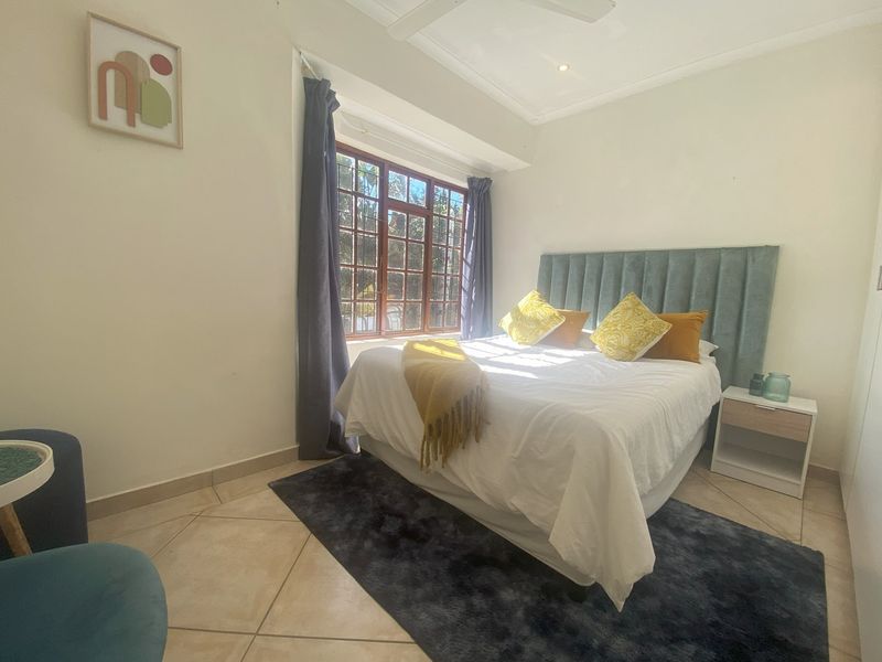 A well-lit bedroom featuring tiled flooring, a ceiling fan, and a large wooden-framed window allowing for natural light.