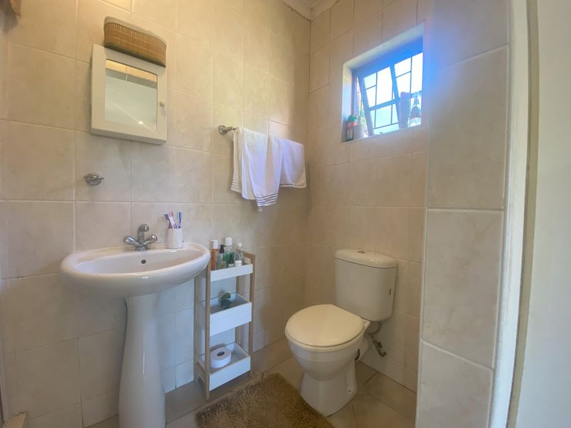 A functional bathroom featuring a pedestal basin, toilet, and neutral wall tiling with a window providing natural light.