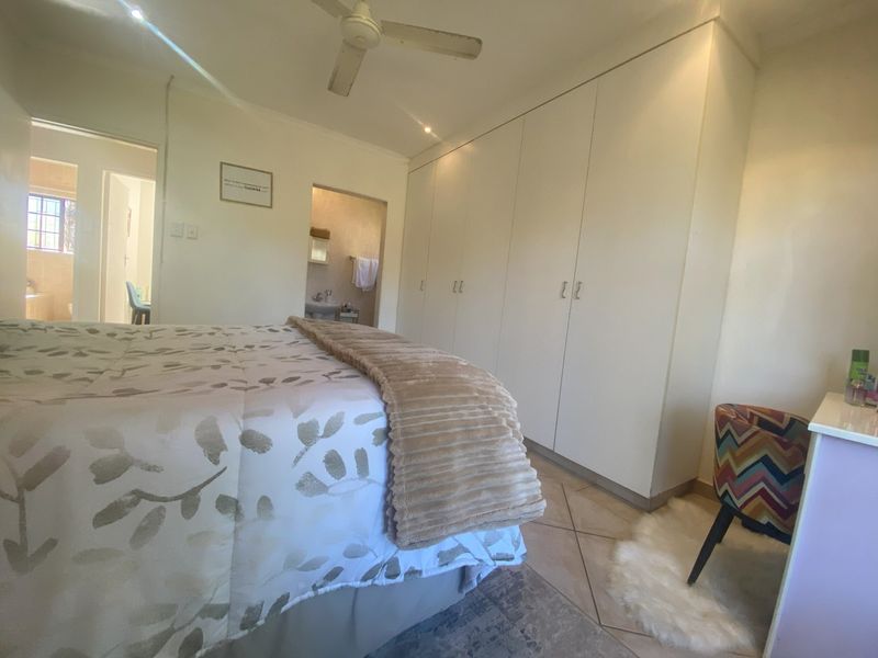 A well-maintained bedroom featuring extensive built-in cupboards, a ceiling fan, and tiled flooring, with convenient access to an adjoining en-suite bathroom.