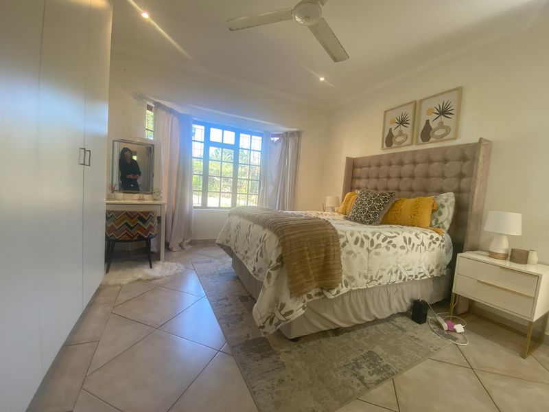 A well-lit bedroom featuring tiled flooring, built-in cupboards, a ceiling fan, and a bay window that allows for natural light.