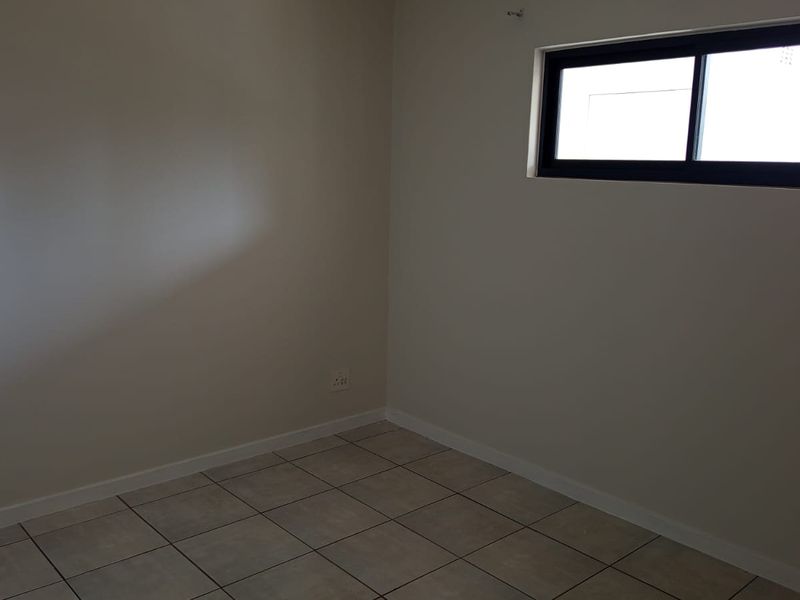 A clean, empty bedroom featuring neutral tiled flooring and a modern sliding window, providing a blank canvas for personalization.