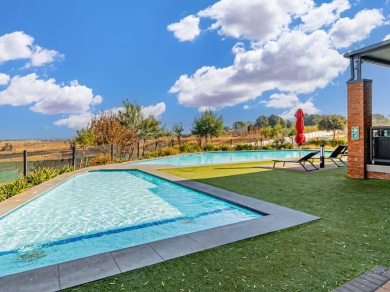 Outdoor pool area featuring a swimming pool, artificial lawn, and a covered patio with brick pillars, offering expansive views of the surrounding landscape.