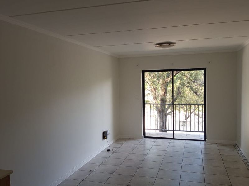 An open-plan living area featuring neutral tiled flooring, clean white walls, and a sliding glass door providing access to a balcony.