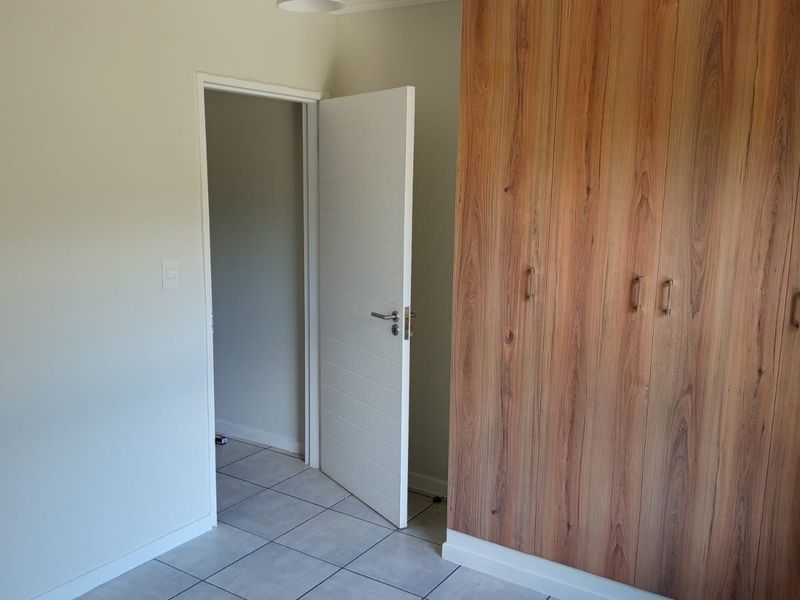 A clean, empty bedroom featuring modern wood-look built-in cupboards and neutral tiled flooring, providing a versatile space ready for personalization.