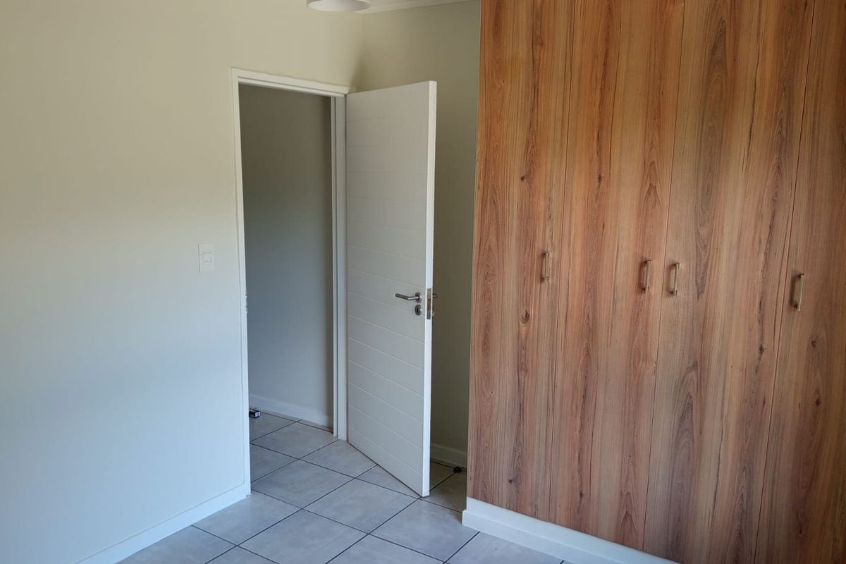 A clean, empty bedroom featuring modern wood-look built-in cupboards and neutral tiled flooring, providing a versatile space ready for personalization.