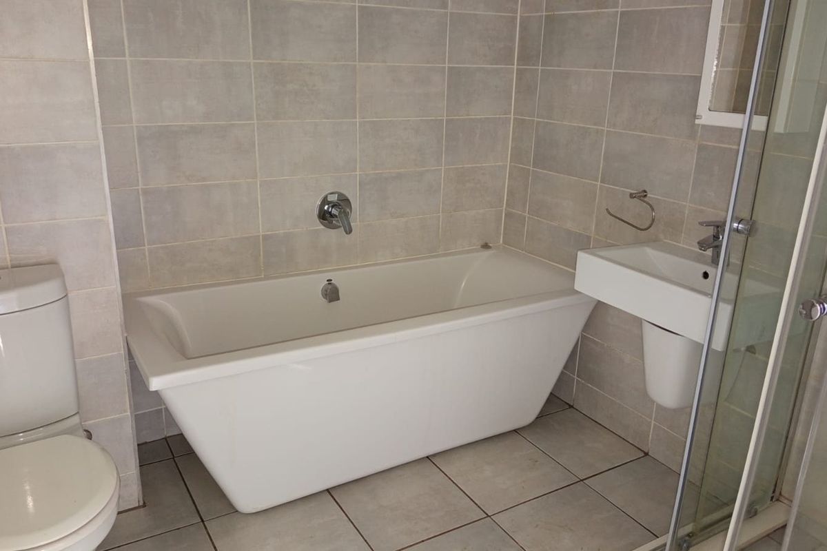 A clean, modern bathroom featuring a white bathtub, wall-mounted basin, toilet, and a glass-enclosed shower with neutral ceramic tiling throughout.