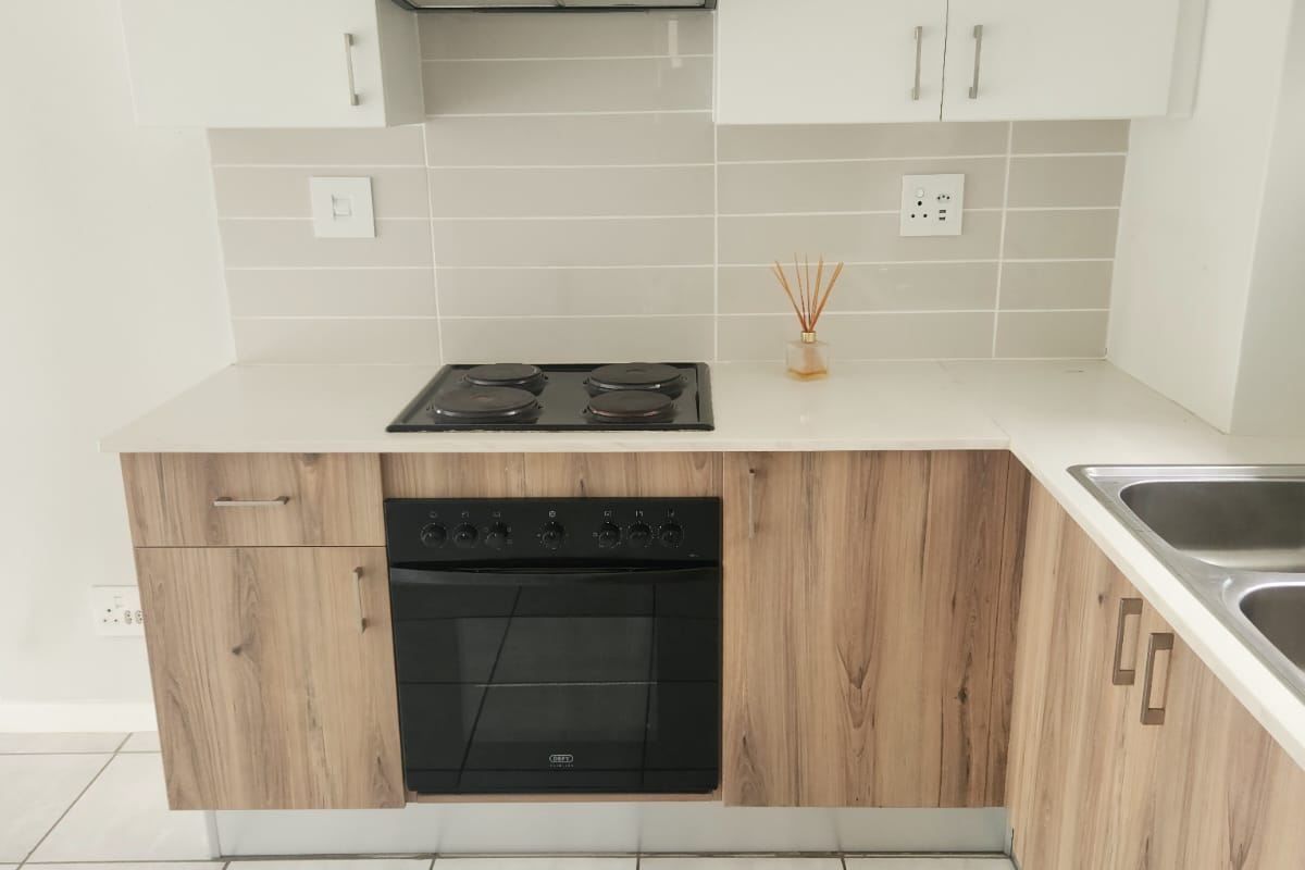 Modern kitchen featuring wood-grain lower cabinets, white upper cabinets, stone countertops, built-in oven, electric hob, extractor fan, and neutral tiled flooring.