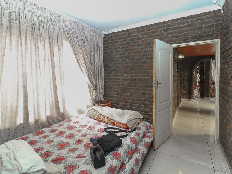 A bedroom featuring exposed brick walls and tiled flooring, with direct access to the hallway.