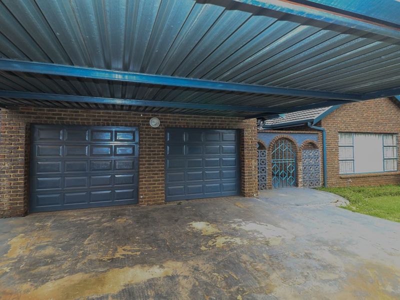 Front exterior view featuring a double garage with a large corrugated metal carport and a decorative security entrance gate.
