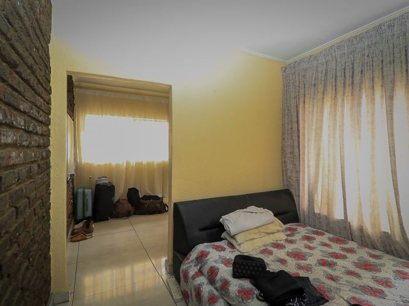 A bedroom featuring tiled flooring and an exposed brick feature wall, with an adjoining space visible through the doorway.