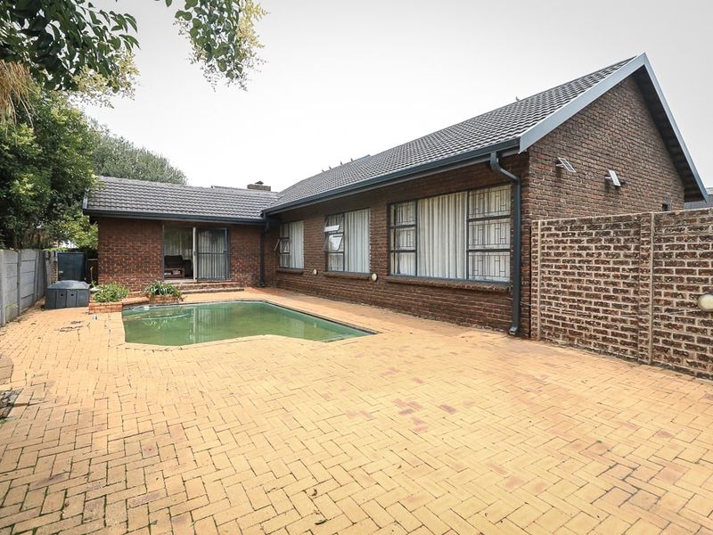 Rear exterior view featuring a facebrick house, paved patio area, and a swimming pool with direct access via sliding glass doors.