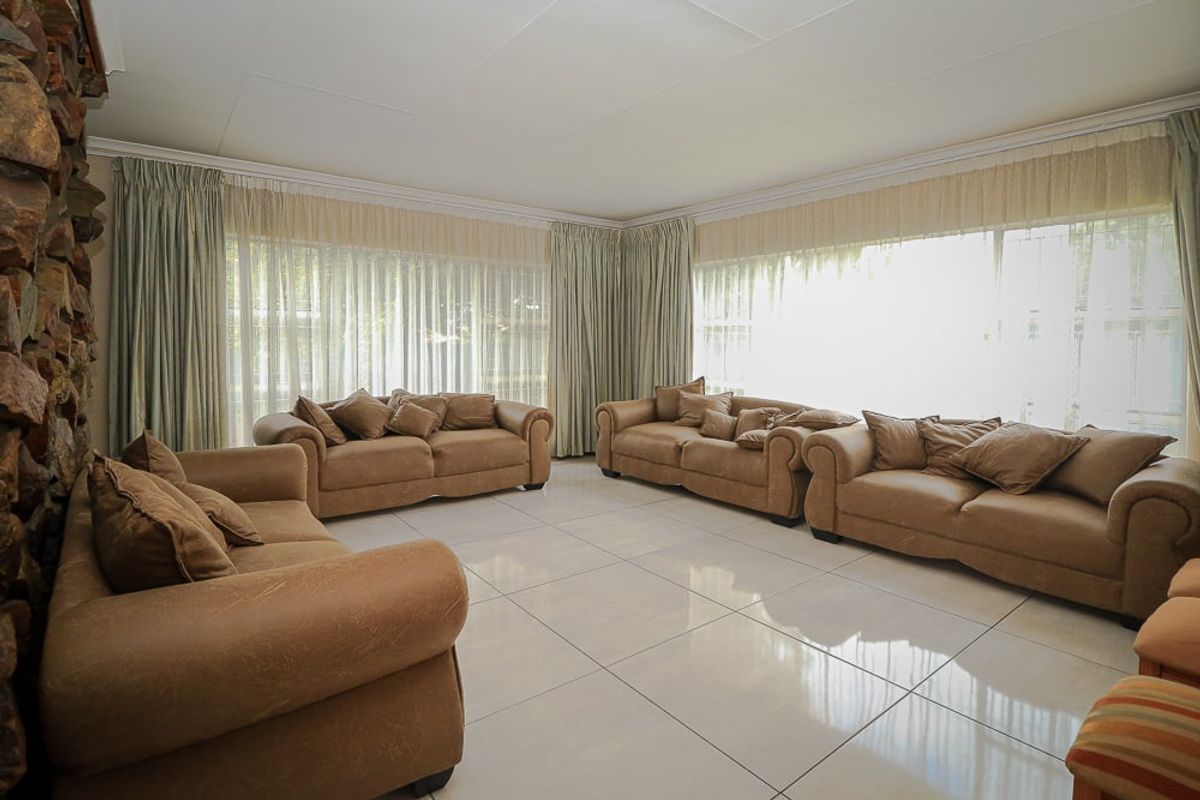 Spacious living room featuring large windows, polished tiled flooring, and a prominent stone fireplace, offering a bright and comfortable area for relaxation.