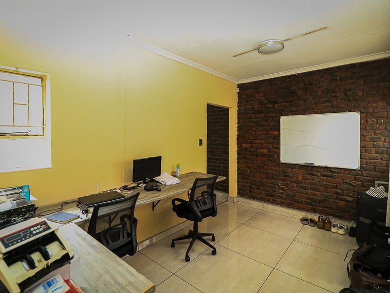 A functional home office space featuring an exposed brick accent wall, ceramic tiled flooring, and a window with security bars.