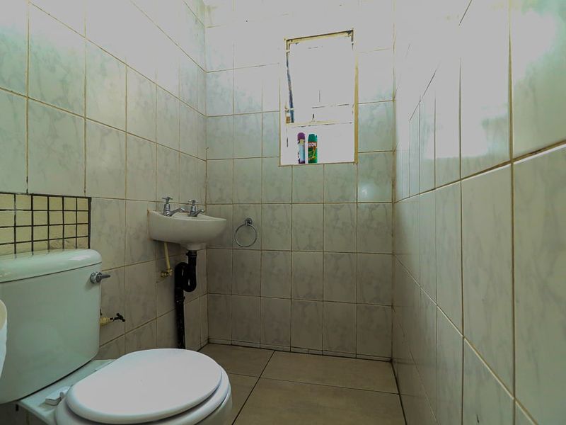 A compact bathroom featuring full-height ceramic wall tiling, a wall-mounted basin, and a standard toilet.