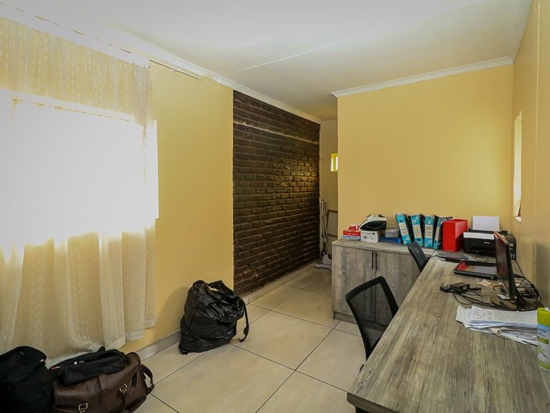 A functional home office space featuring tiled flooring, a built-in desk, and a distinctive exposed brick feature wall.