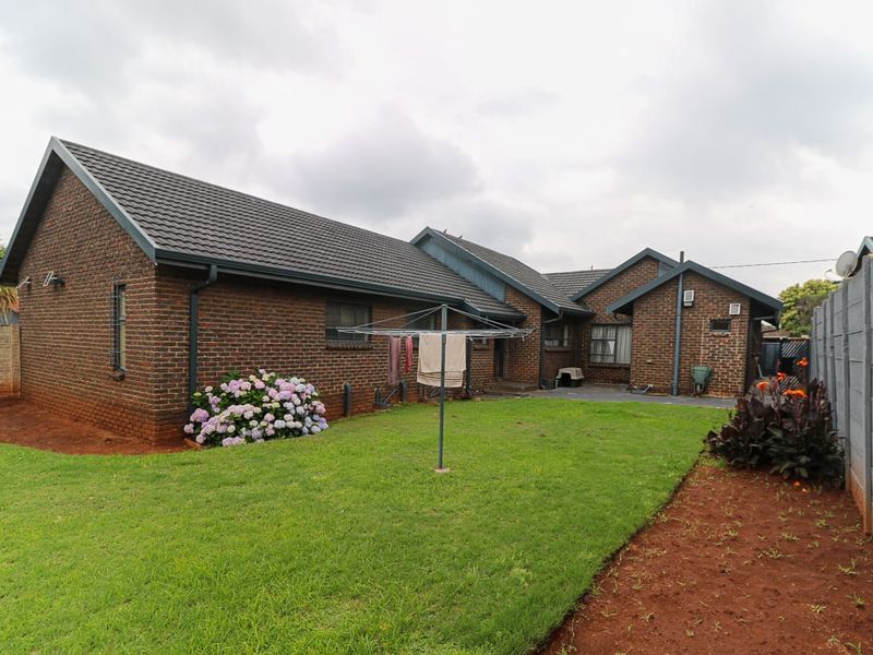 Rear view of the brick house featuring a tiled roof, gutters, and a spacious garden with a precast concrete boundary wall.