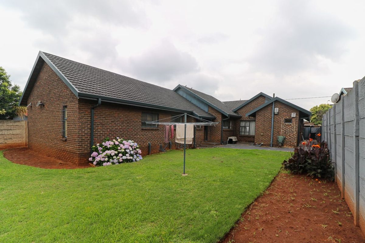 Rear view of the brick house featuring a tiled roof, gutters, and a spacious garden with a precast concrete boundary wall.