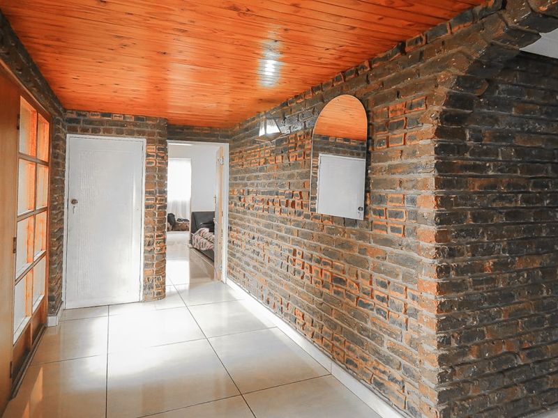 A spacious hallway featuring exposed brick walls, a warm timber ceiling, and neutral ceramic floor tiles, providing a rustic and character-filled transition space.