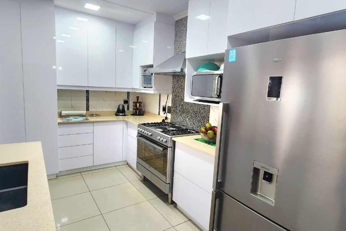 Modern kitchen featuring sleek white cabinetry, stone countertops, stainless steel gas stove, extractor fan, and high-quality tiled flooring.
