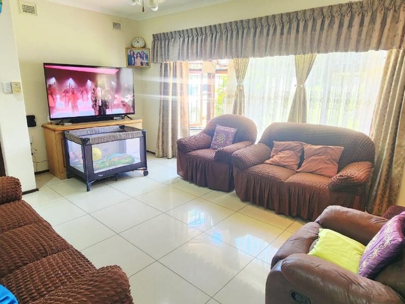 A spacious living room featuring neutral tiled flooring, decorative cornice, and a large window with a fitted curtain pelmet.