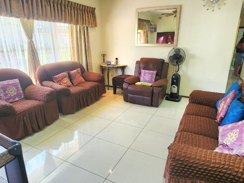 A spacious living room featuring large windows with curtain pelmets and neutral tiled flooring, offering a bright and functional family living space.