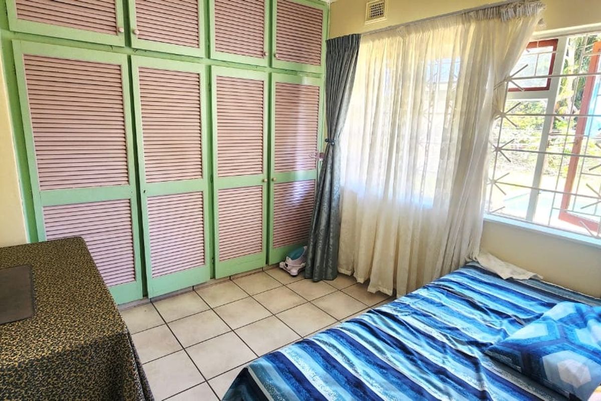 A bedroom featuring built-in cupboards with louvered doors, tiled flooring, and a window fitted with security bars.