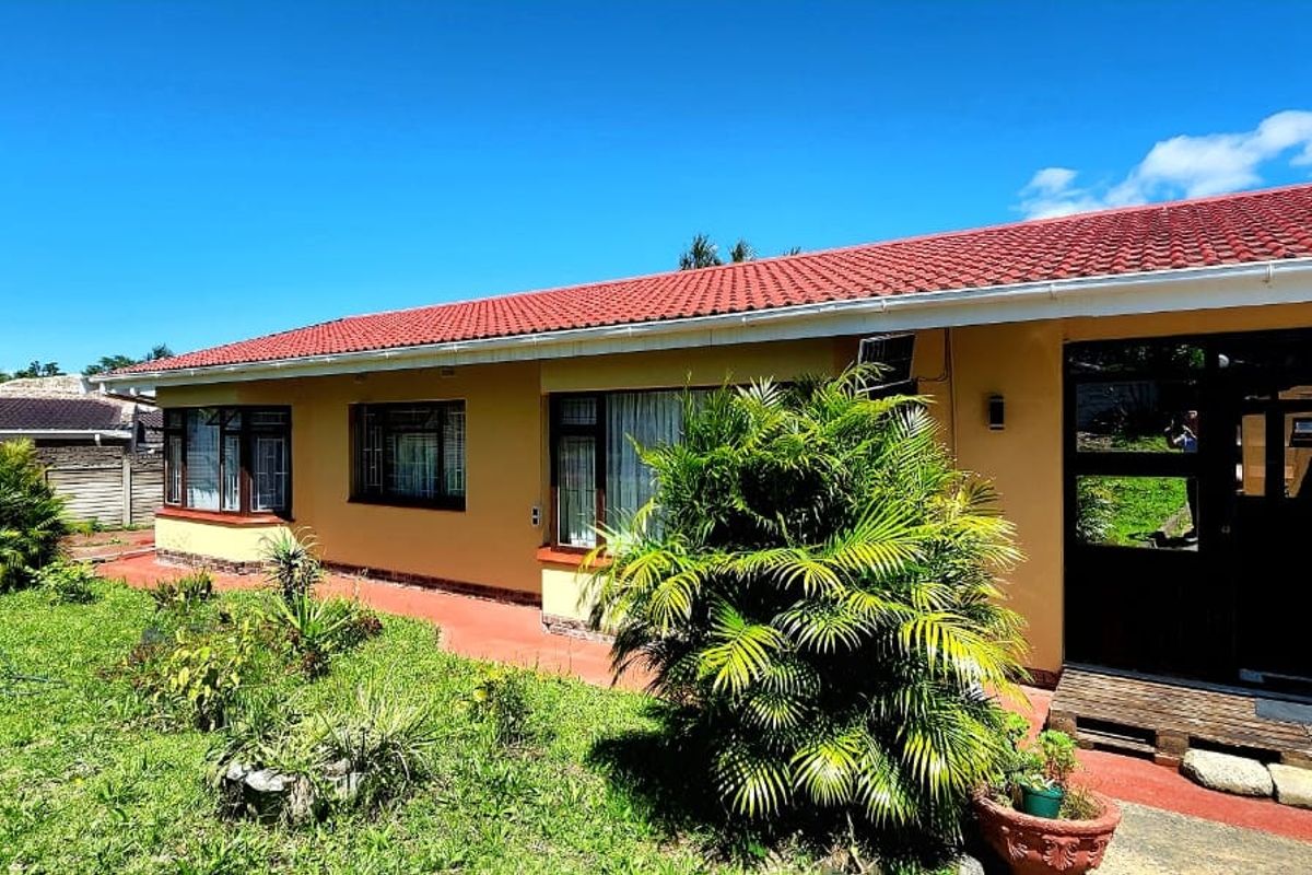Rear view of a single-story house featuring a tiled roof, brick facade, and large windows overlooking a garden area.