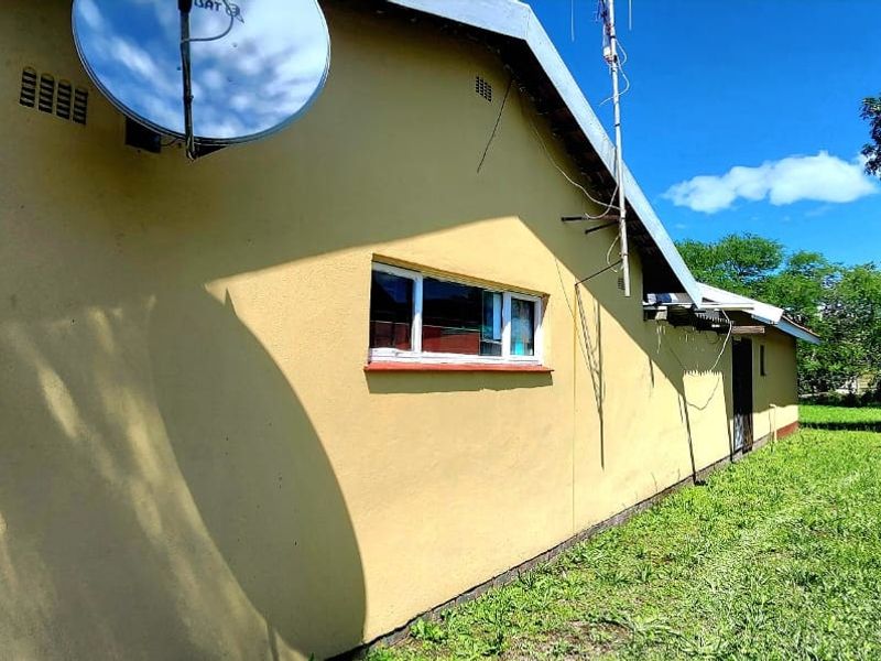 Rear exterior view of the property showing the side facade, satellite dish, and grassed backyard area with boundary walling.
