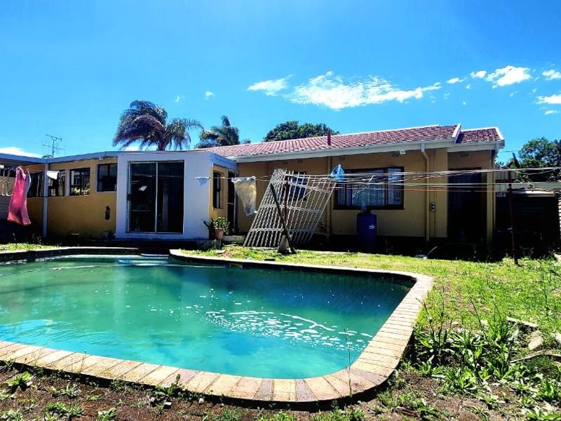 Rear exterior view of the property featuring a swimming pool with brick coping, a tiled roof, and a fenced garden area.