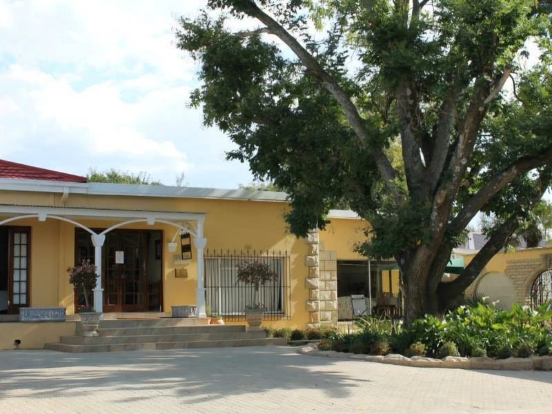 Front elevation of a single-story residence featuring a paved driveway, covered veranda with decorative columns, and established garden landscaping.