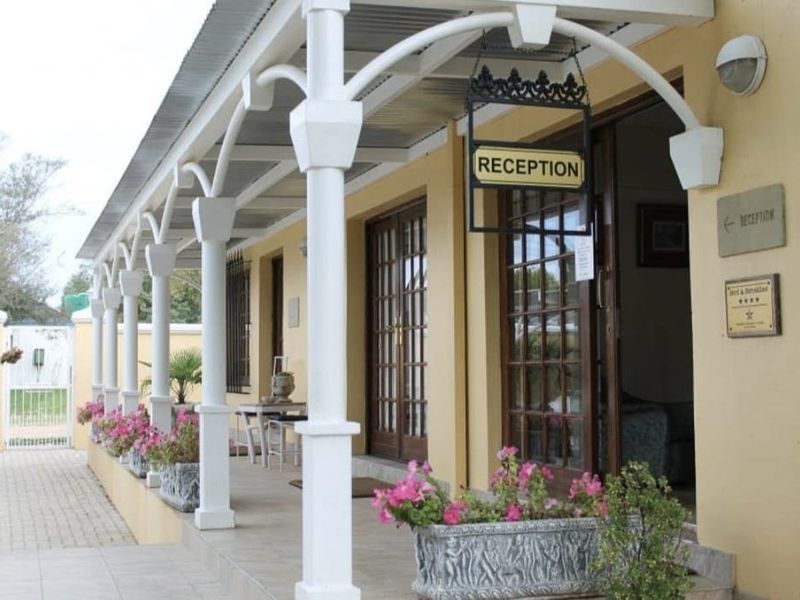 A well-maintained covered veranda featuring decorative columns, tiled flooring, and timber-framed glass entrance doors, providing a welcoming exterior access point.