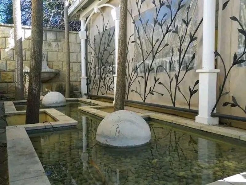 A tranquil outdoor water feature area featuring stone masonry, decorative metal screens, and integrated water basins with built-in architectural columns.