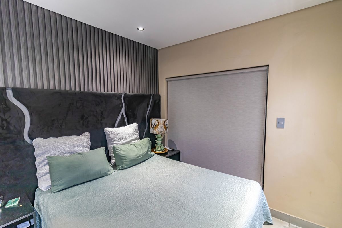 A well-maintained bedroom featuring a modern textured feature wall, recessed downlighting, and a fitted roller blind for privacy.
