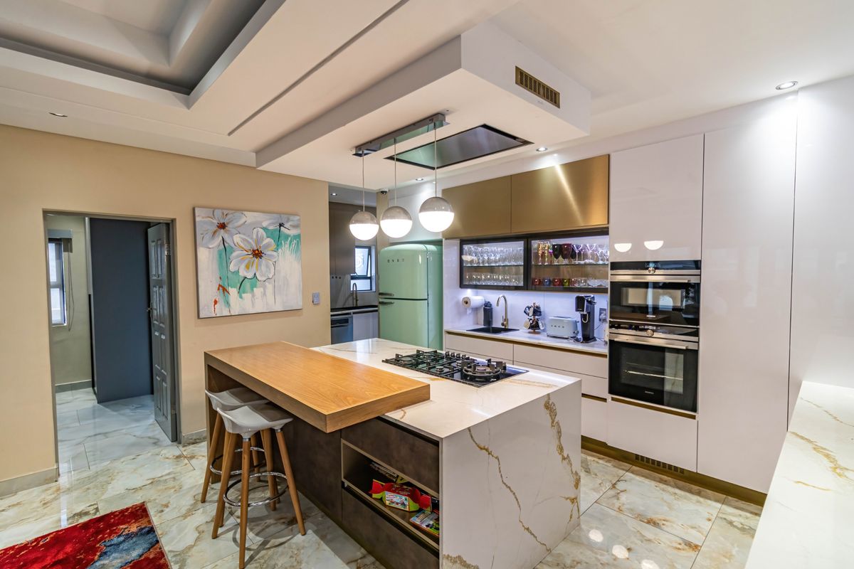 Modern kitchen featuring a central island with gas hob, stone countertops, integrated appliances, and high-end marble-look flooring with sophisticated recessed ceiling lighting.