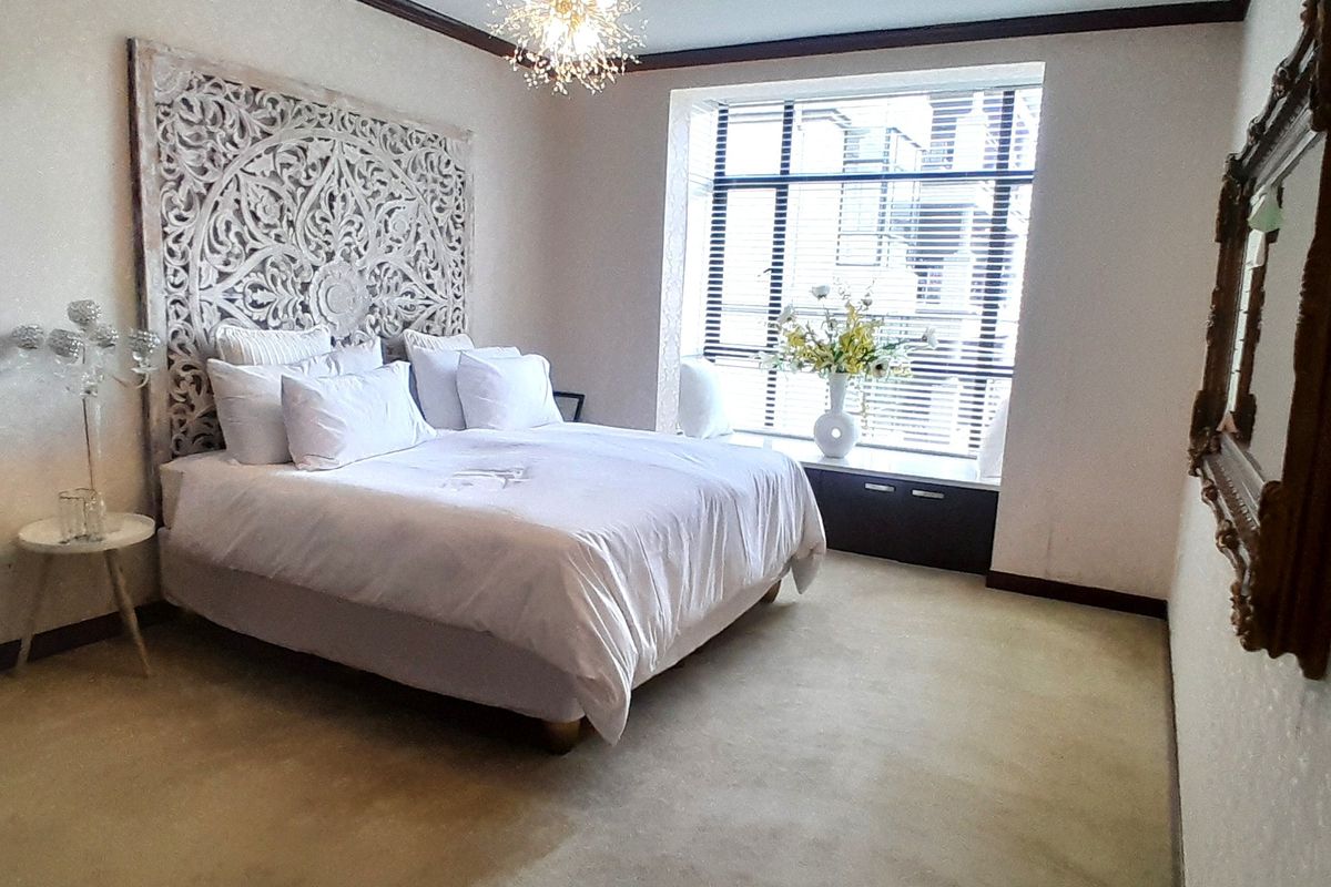 A well-lit bedroom featuring neutral carpeting, crown molding, and a built-in window seat with venetian blinds.