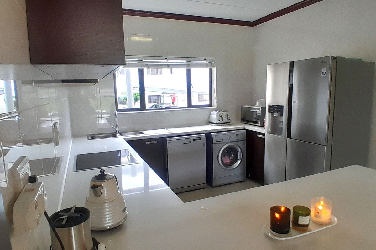 A functional kitchen featuring white quartz countertops, dark cabinetry, a built-in electric cooktop, and integrated space for laundry and dishwashing appliances.