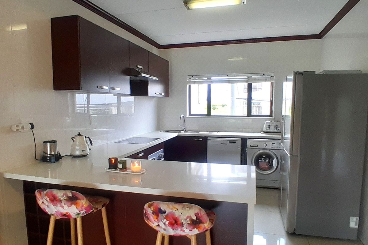 Modern kitchen featuring dark wood cabinetry, white quartz countertops, a breakfast bar, and integrated appliances with a clean tiled finish.