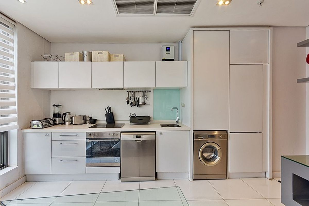 Modern compact kitchen featuring white cabinetry, integrated appliances including a dishwasher and washing machine, glass splashback, and sleek tiled flooring.