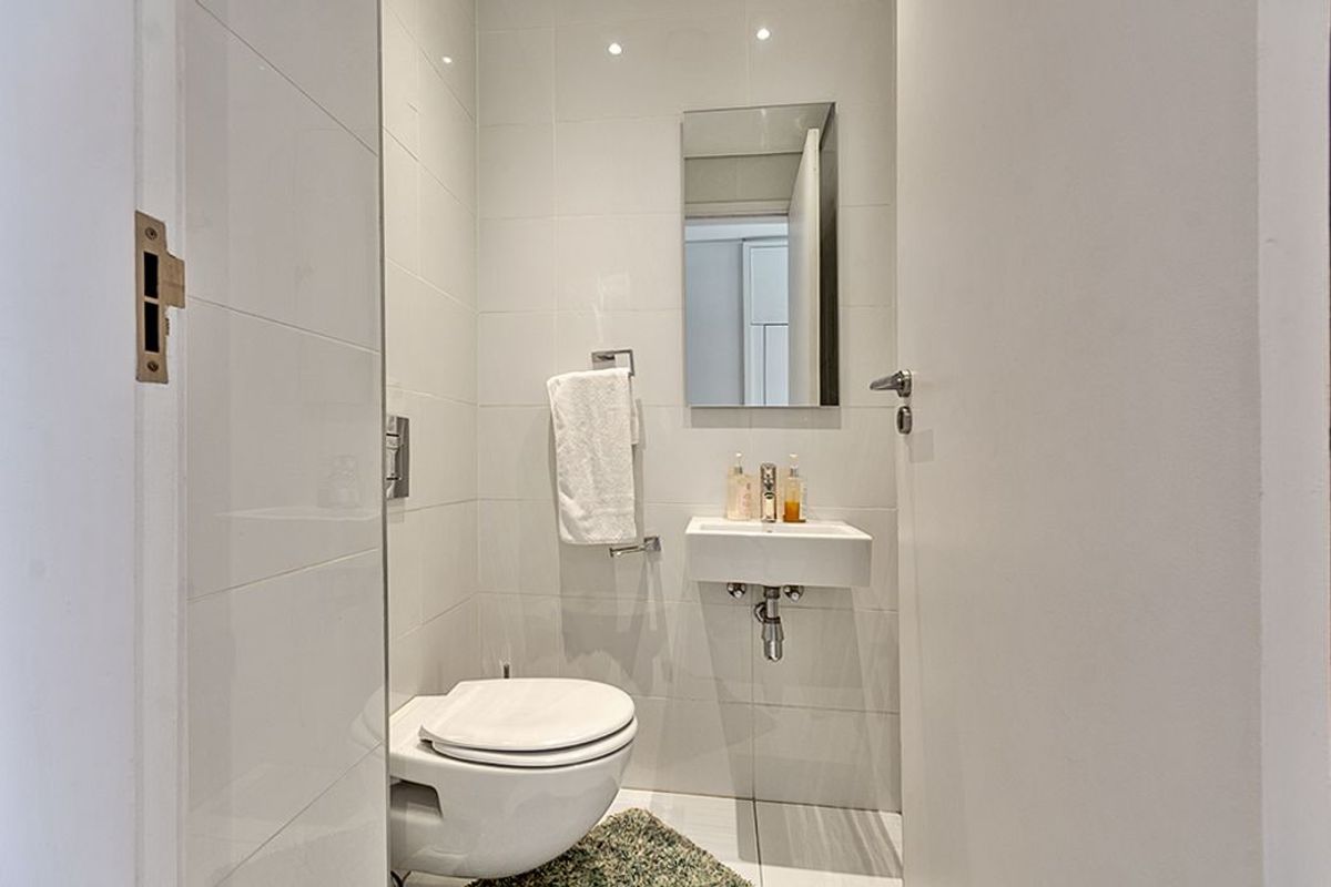 A compact, modern guest bathroom featuring a wall-mounted toilet, sleek wall-mounted basin, and neutral tiled finishes.
