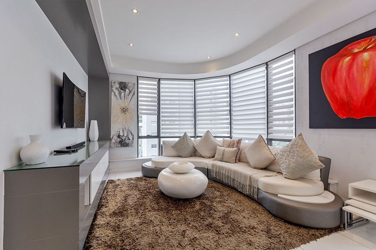Modern living room featuring a curved window wall with integrated blinds, recessed ceiling lighting, and a sleek built-in media console.