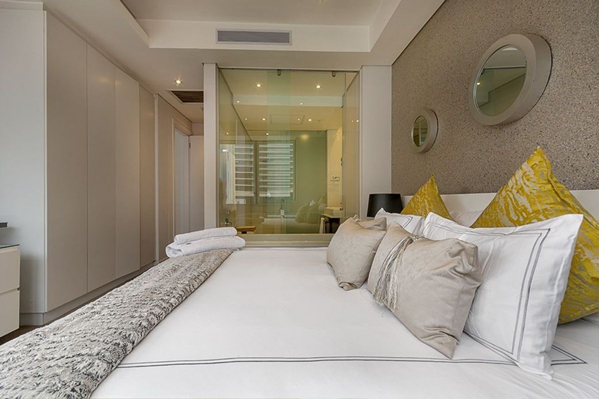 Modern bedroom featuring built-in cupboards, a textured feature wall, and a contemporary glass-enclosed en-suite bathroom with integrated lighting.