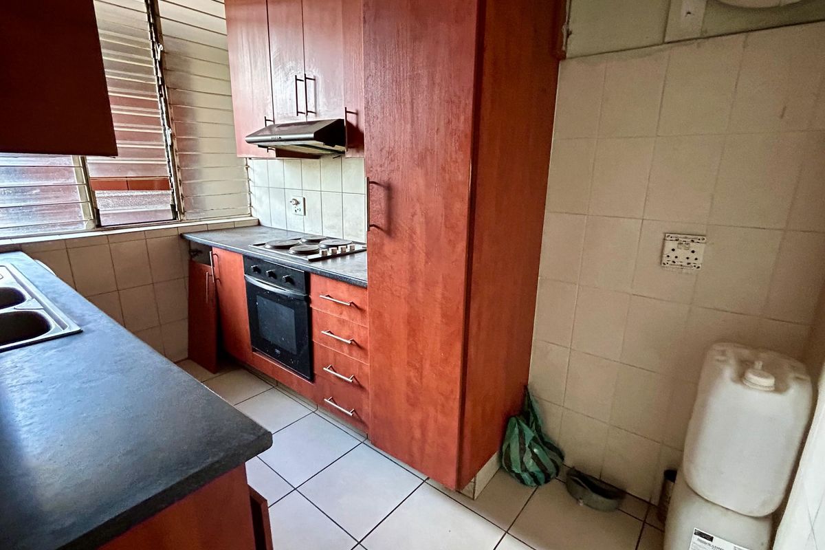 A dated kitchen featuring wood-tone cabinetry, built-in oven and hob, tiled splashbacks, and tiled flooring, offering potential for a modern renovation.