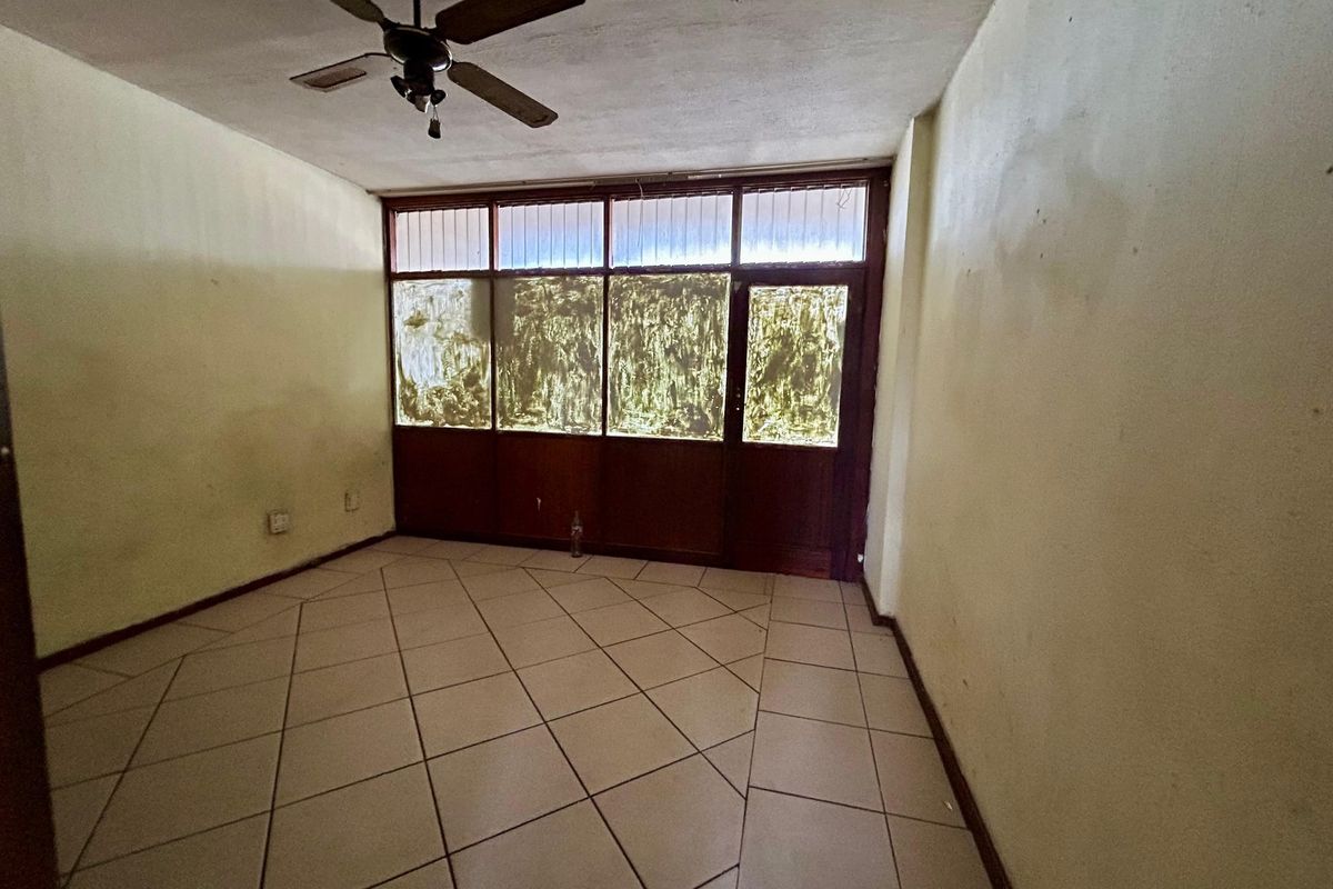 An empty living room featuring tiled flooring, a ceiling fan, and large window panels with a glass door leading to an exterior space.